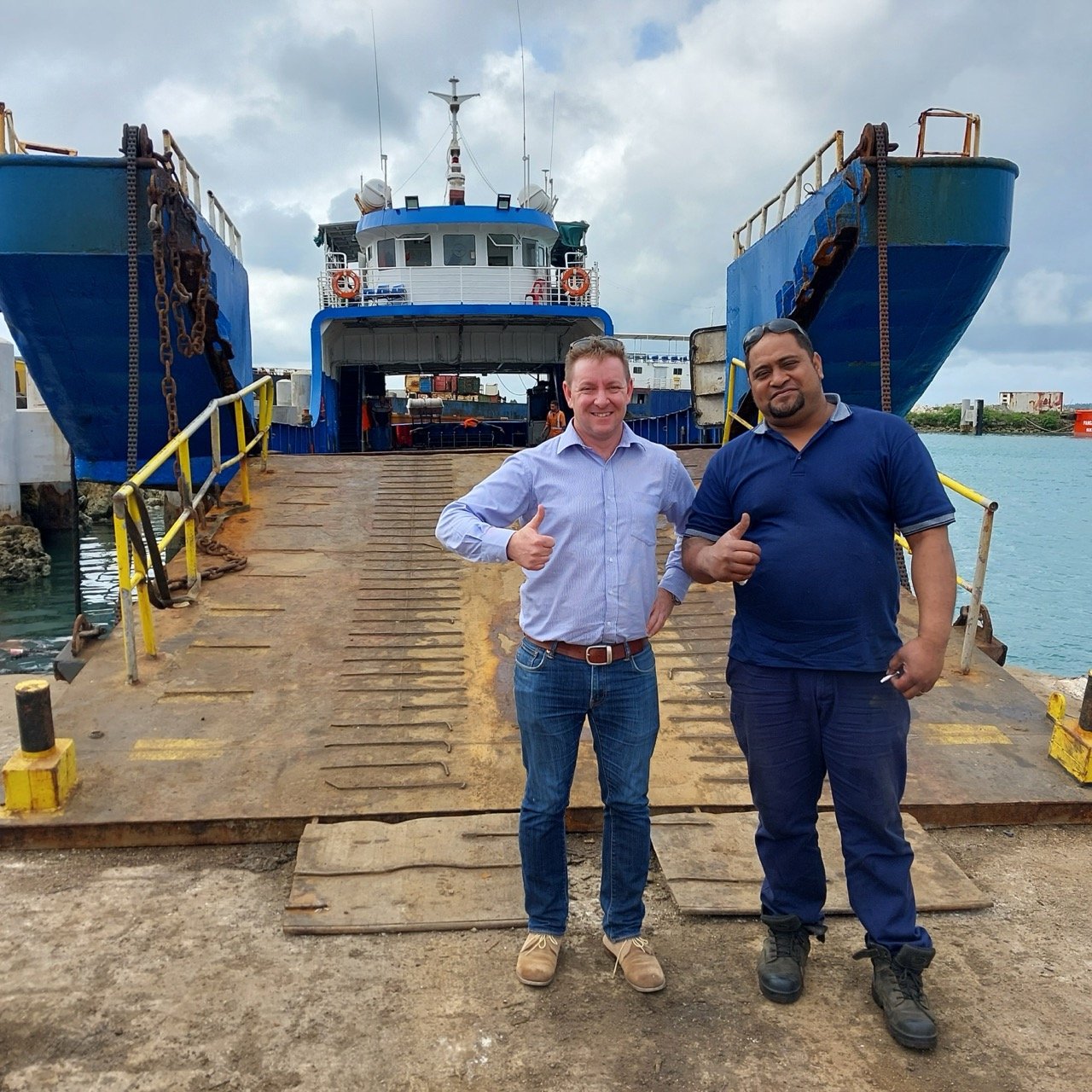 two men standing in front of barge in the pacific islands